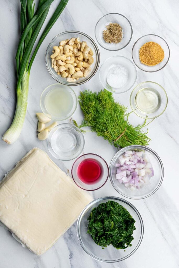ingredients for Greek spinach spanakopita including spinach, herbs, cashews, olive oil, and phyllo dough