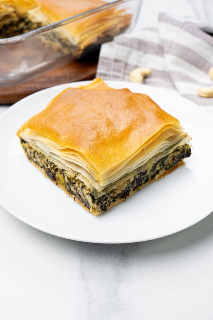 Served slice of vegan greek spinach pie on a plate with flaky phyllo, spinach, and cashew feta