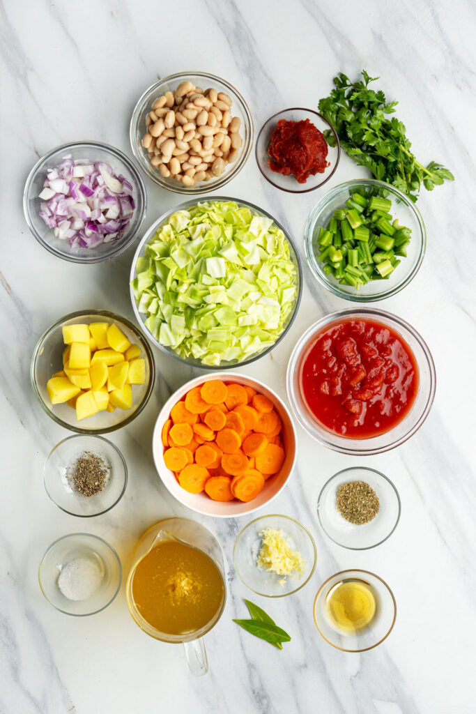 ingredients for vegan cabbage soup including potatoes, carrots, and white beans