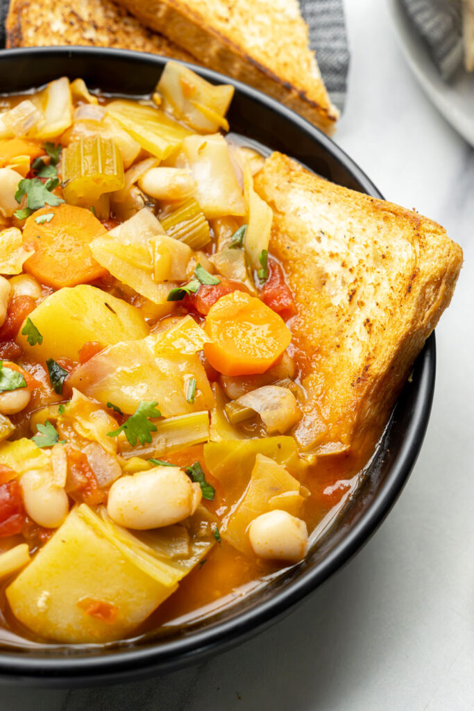 close up of plant-based cabbage soup served with crusty bread in a black bowl