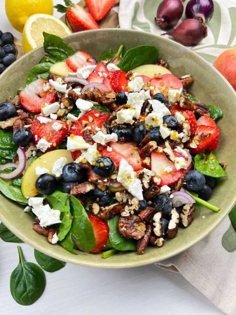close up view vegan mixed berry salad with spinach, strawberries, red onions, and candies pecans