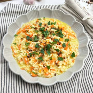 Easy carrot risotto topped with crispy shallots and herbs in a while bowl close up