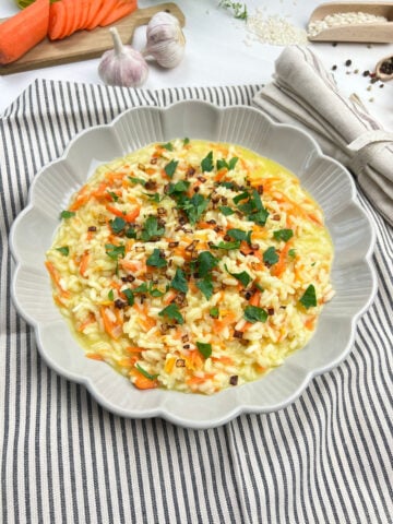 Easy carrot risotto topped with crispy shallots and herbs in a while bowl close up