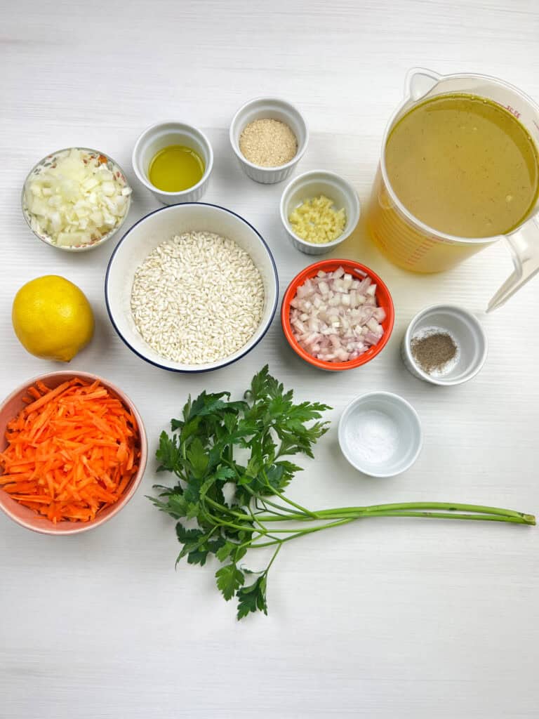Ingredients for carrot risotto including arborio rice, shredded carrots, broth, vegetables, and herbs