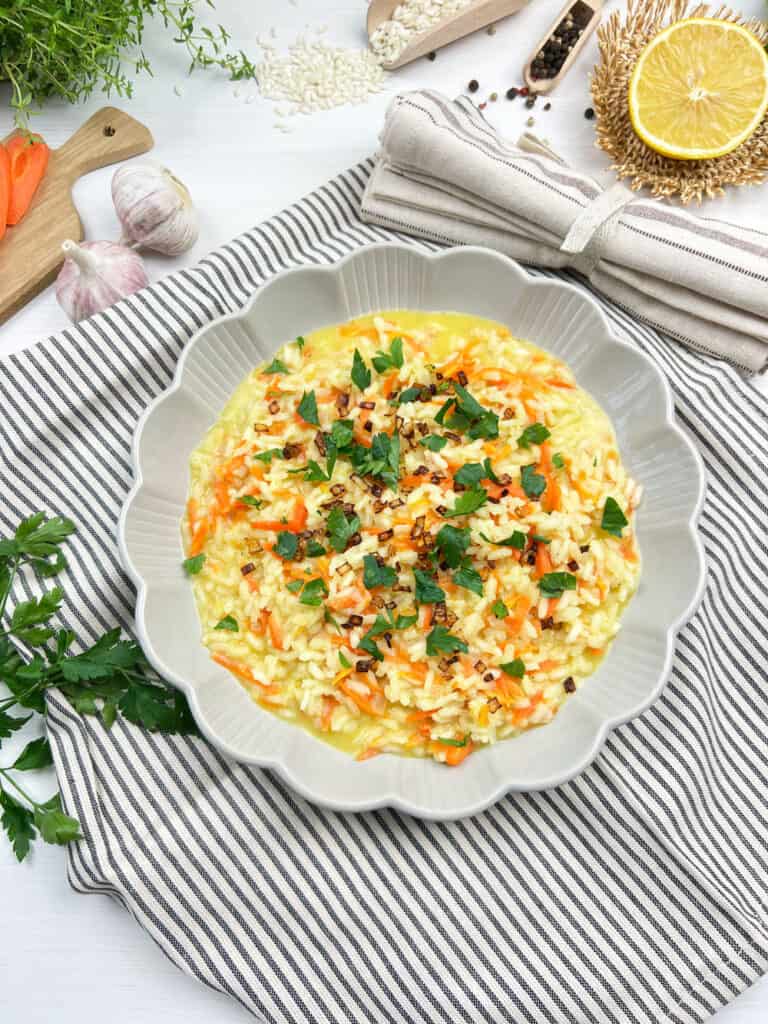 Creamy vegan carrot risotto topped with crispy shallots and parsley in a white bowl