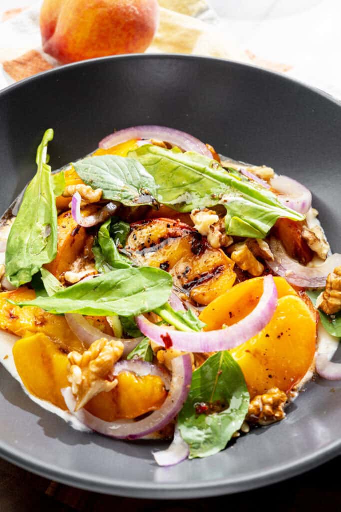 close up of grilled stone fruit salad with vegan whipped feta, fresh basil, and walnuts in a bowl