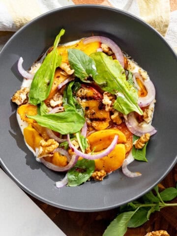 grilled vegan peach salad with basil, walnuts and red onion sitting on dairy-free whipped feta