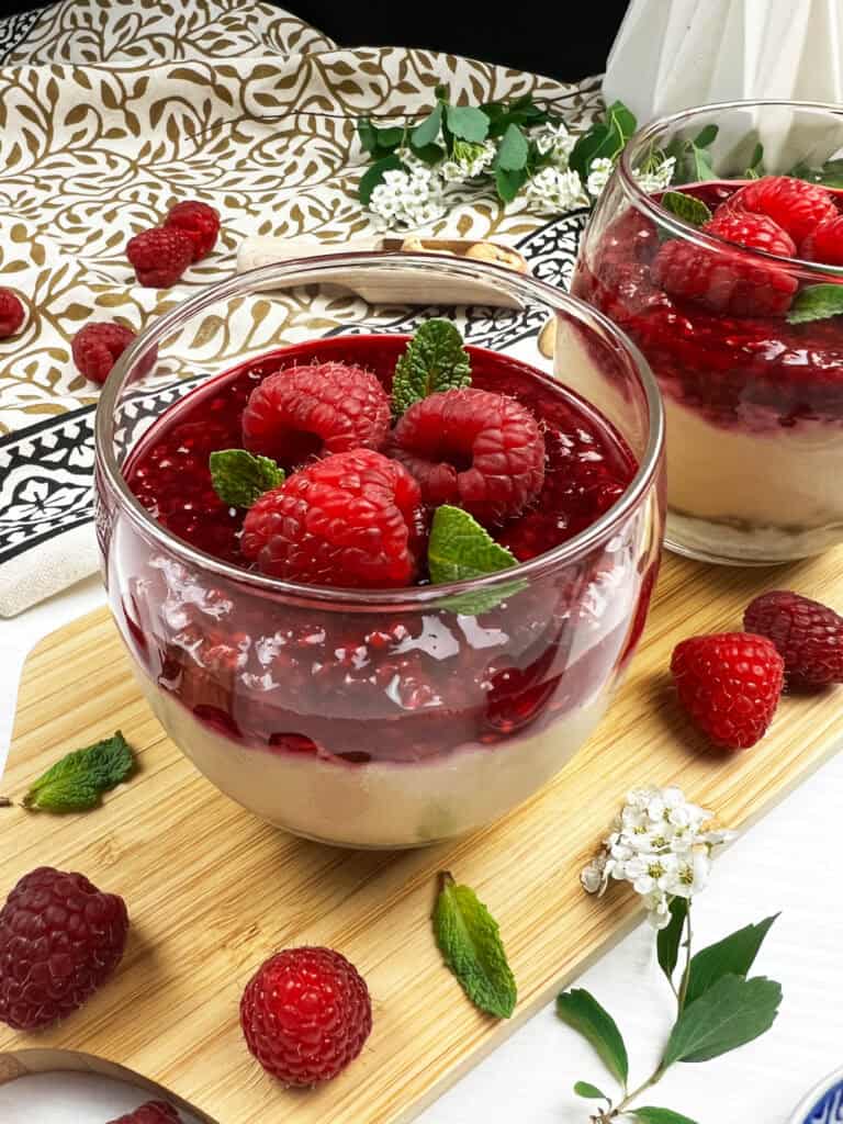 Close-up of a creamy vegan cheesecake cup topped with a raspberry compote and fresh mint