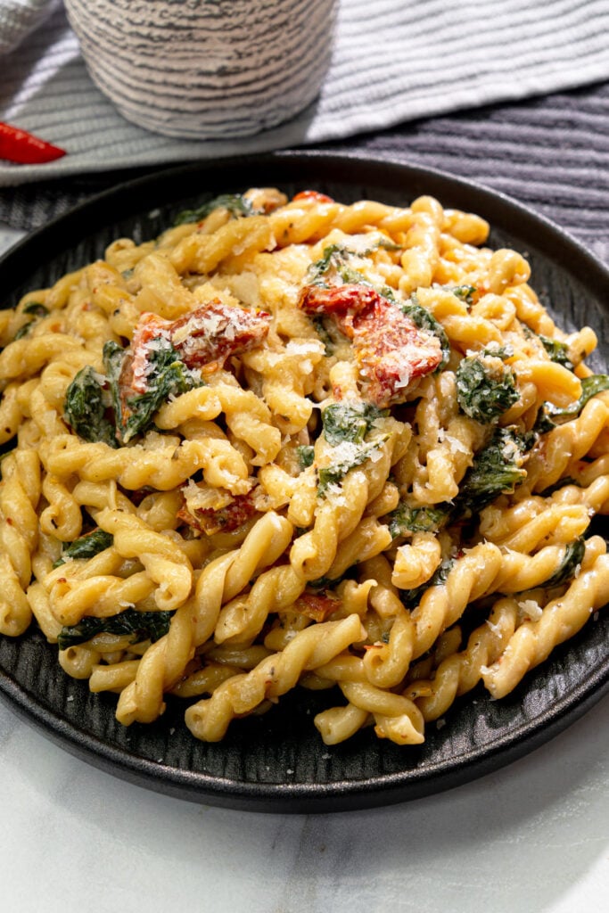 Creamy Tuscan pasta with sun dried tomatoes, spinach, and gemelli pasta in a black bowl