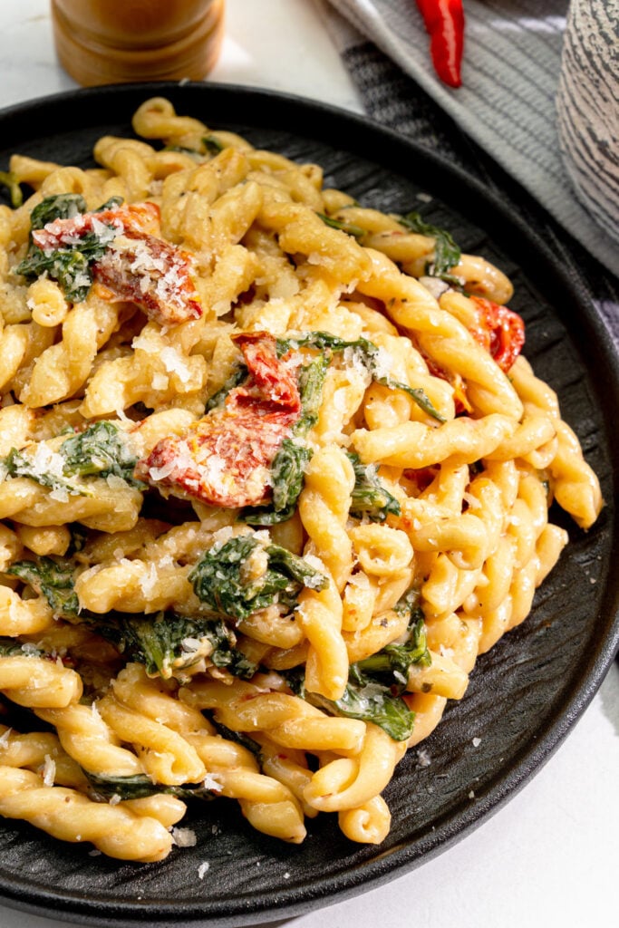 Close-up of creamy vegan sun dried tomato pasta with spinach and gemelli noodles
