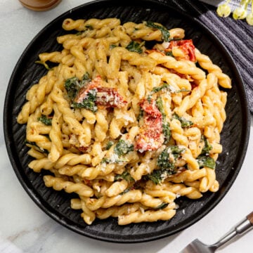 creamy vegan Tuscan pasta with spinach, sun-dried tomatoes, and vegan parmesan in a black bowl