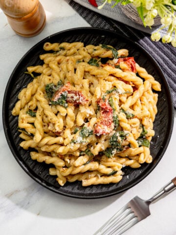 creamy vegan Tuscan pasta with spinach, sun-dried tomatoes, and vegan parmesan in a black bowl