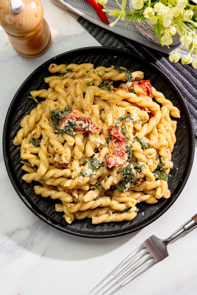creamy vegan Tuscan pasta with spinach, sun-dried tomatoes, and vegan parmesan in a black bowl