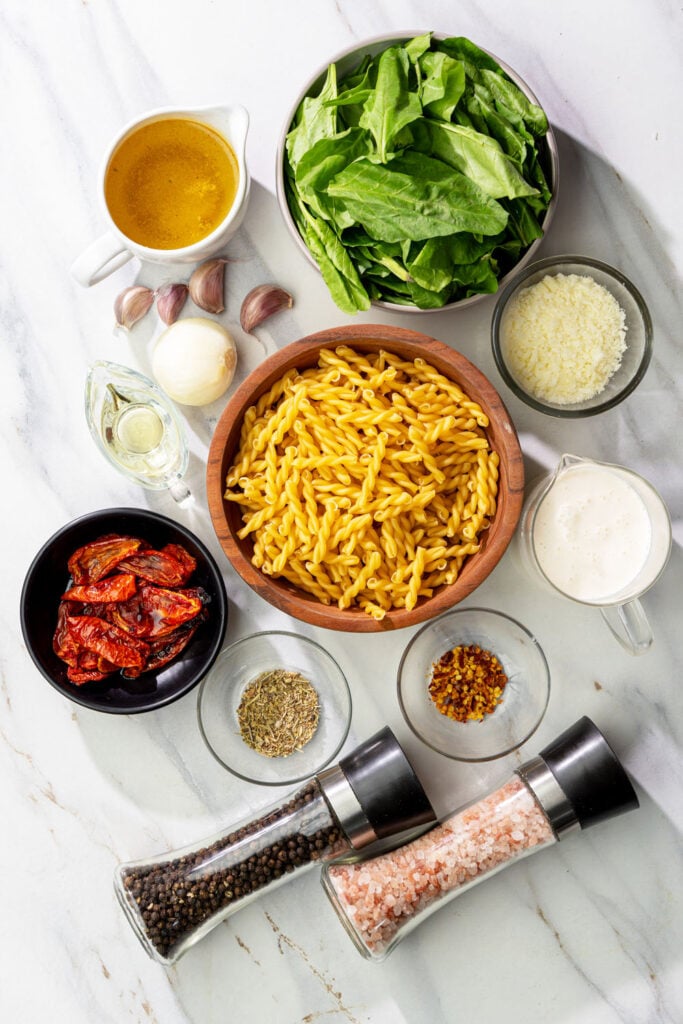 Ingredients for vegan Tuscan sun dried tomato pasta including gemelli, spinach, garlic, and dairy-free parmesan