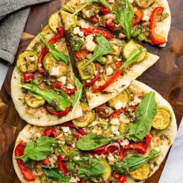 vegan chimichurri flatbread with grilled vegetables, dairy-free feta, and arugula sliced on a wood board