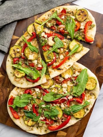 vegan chimichurri flatbread with grilled vegetables, dairy-free feta, and arugula sliced on a wood board