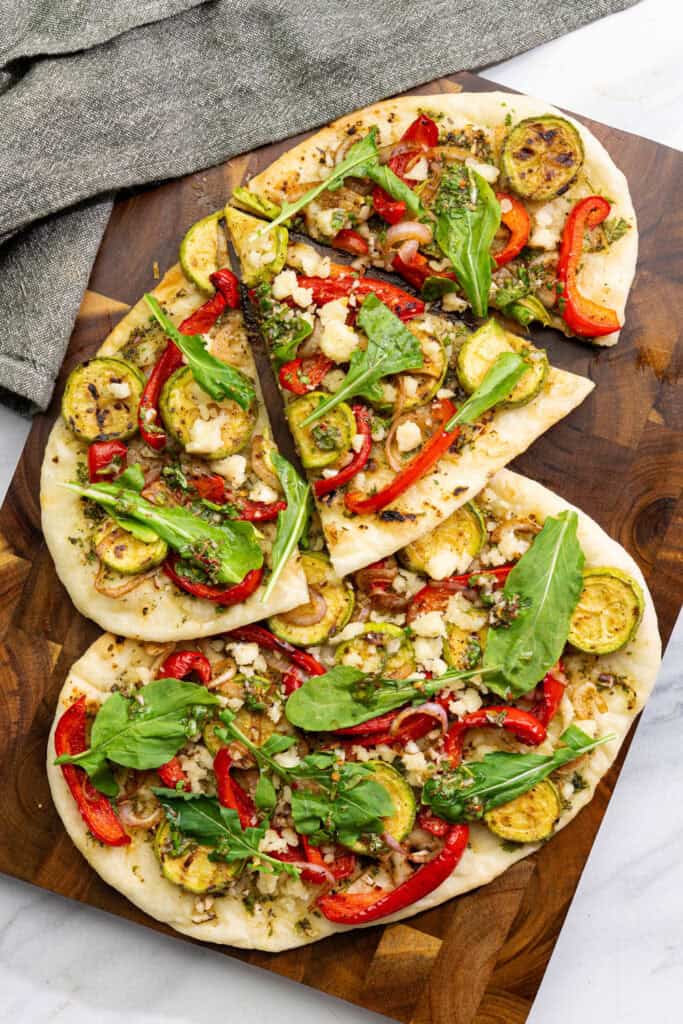 vegan chimichurri flatbread with grilled vegetables, dairy-free feta, and arugula sliced on a wood board