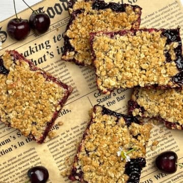 Cherry crumb bars arranged on parchment with fresh fruit and golden oat crumble topping