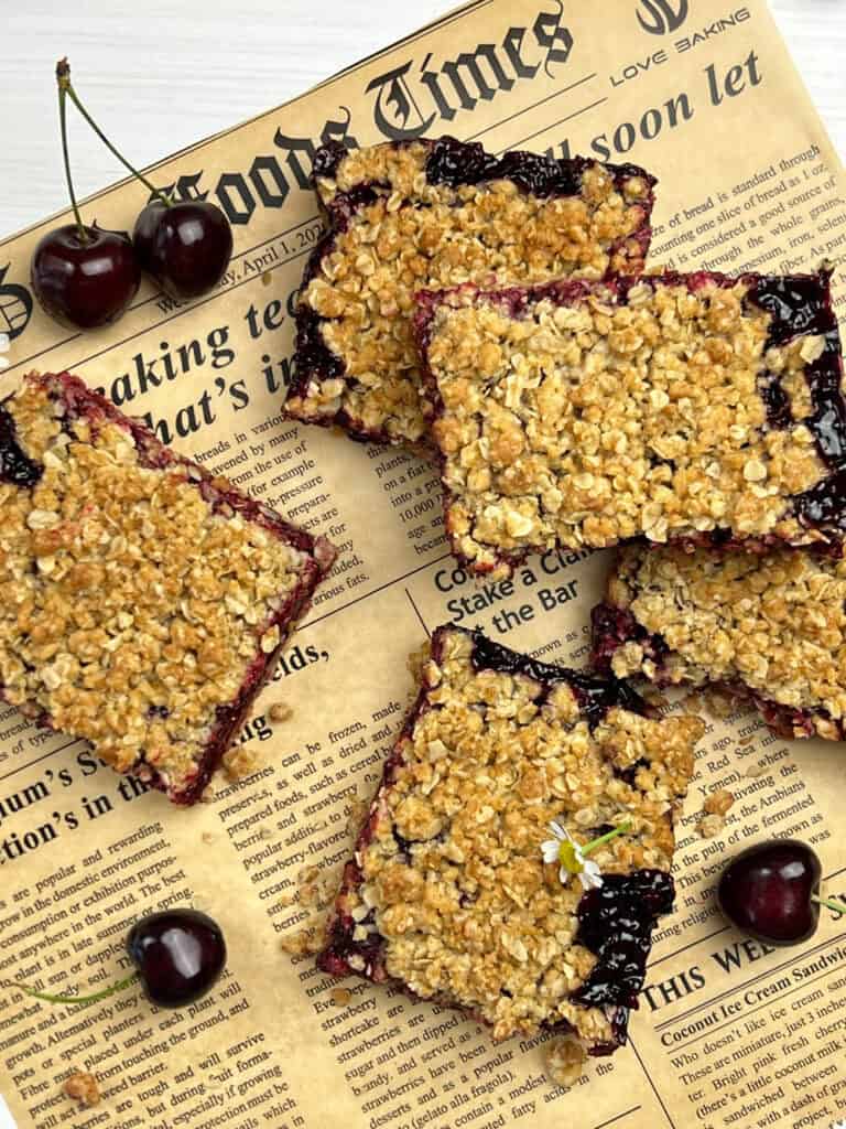 Cherry crumb bars arranged on parchment with fresh fruit and golden oat crumble topping