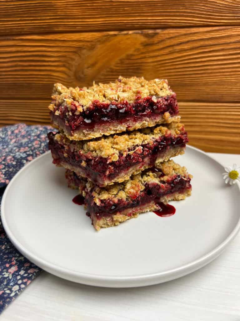 Stacked vegan crumb bars on a white plate with a buttery oat topping and juicy cherry filling