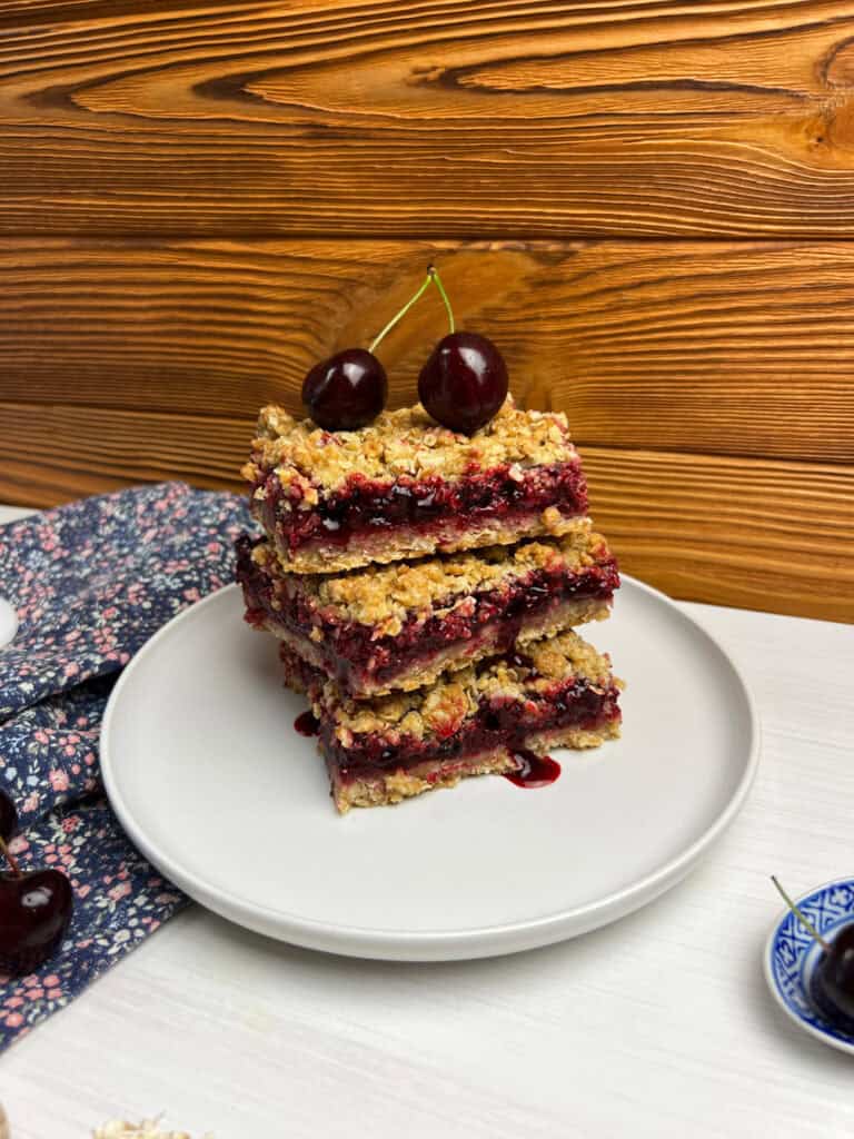 side view of homemade cherry bars stacked on a plate with golden oat crumble