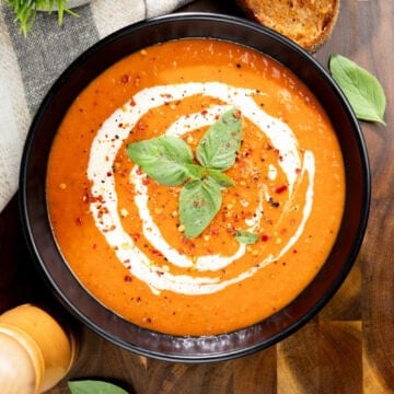 Creamy roasted red pepper soup topped with a swirl of vegan cream, fresh basil and cracked pepper