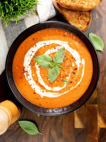 Creamy roasted red pepper soup topped with a swirl of vegan cream, fresh basil and cracked pepper