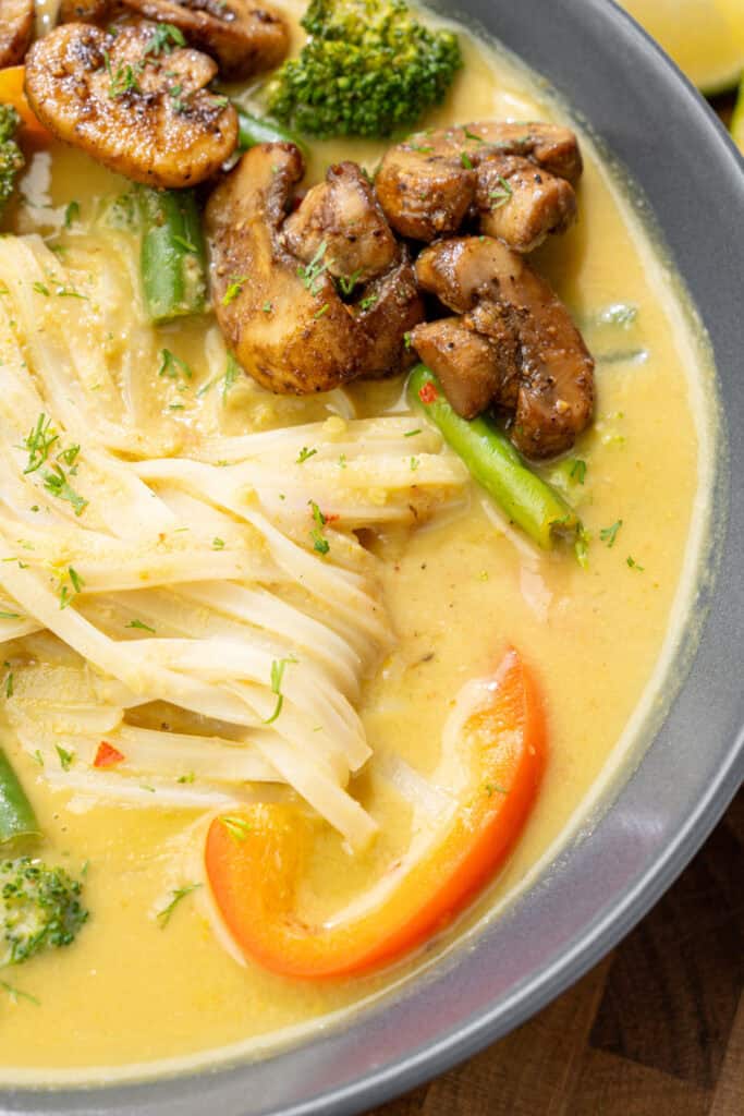 extreme close-up of creamy mango curry noodle soup with rice noodles and veggies