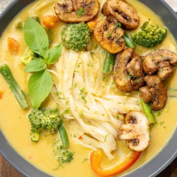Bowl of creamy mango curry noodle soup topped with sauteed mushrooms and other fresh veggies