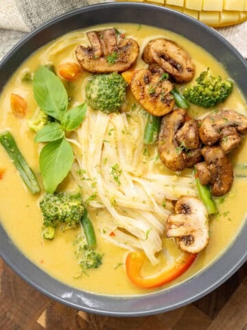 Bowl of creamy mango curry noodle soup topped with sauteed mushrooms and other fresh veggies