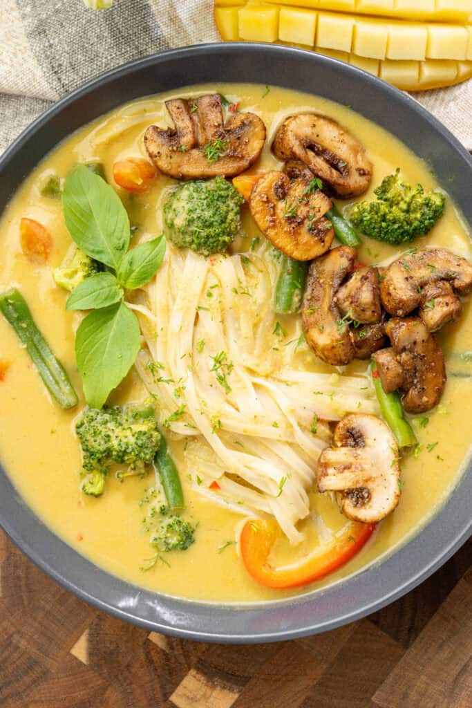 Bowl of creamy mango curry noodle soup topped with sauteed mushrooms and other fresh veggies