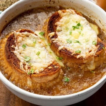 Hot bowl of French onion soup with caramelized onions and topped with dairy-free cheesy baguettes
