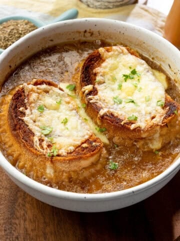 Hot bowl of French onion soup with caramelized onions and topped with dairy-free cheesy baguettes