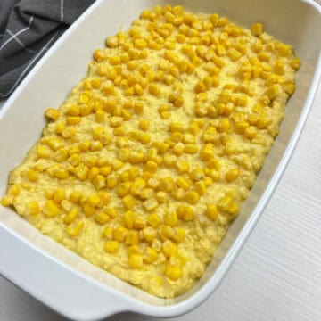 close-up of homemade corn casserole in a white baking dish topped with golden kernals