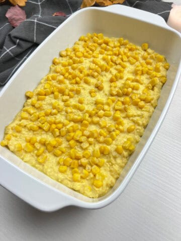close-up of homemade corn casserole in a white baking dish topped with golden kernals