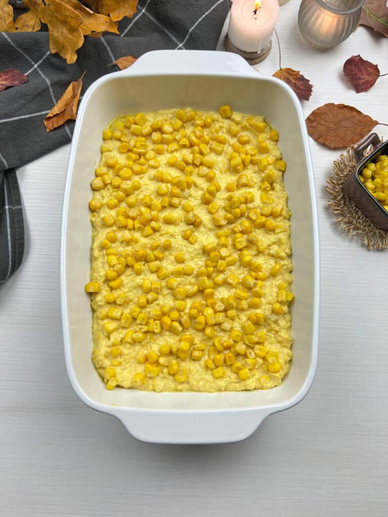 overhead shot of creamy corn casserole in a white baking dish surrounded by autumn leaves