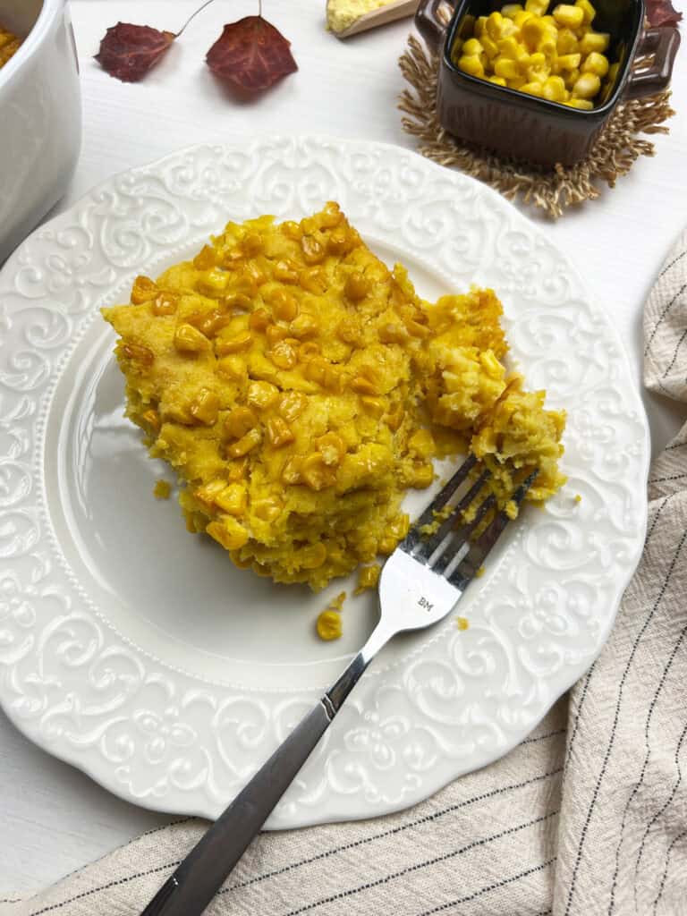 A generous serving of creamy baked corn dish on a white plate with a fork