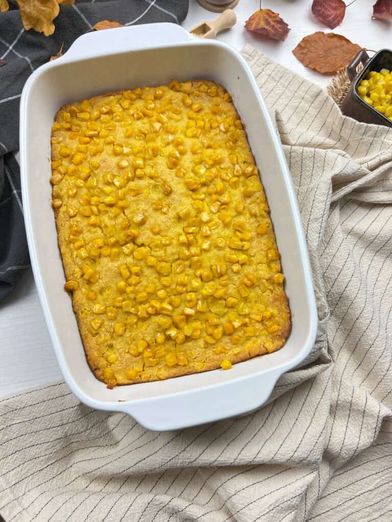 golden creamy vegan corn casserole baked in a white ceramic dish with cozy autumn styling