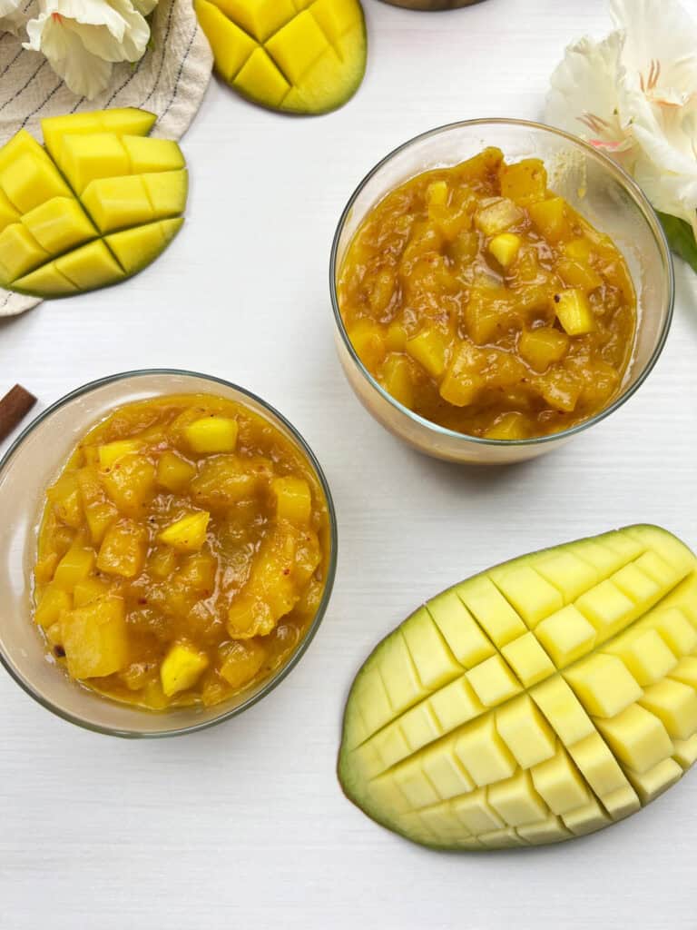 2 bowls of chunky homemade mango chutney served alongside freshly cut ripe mangos