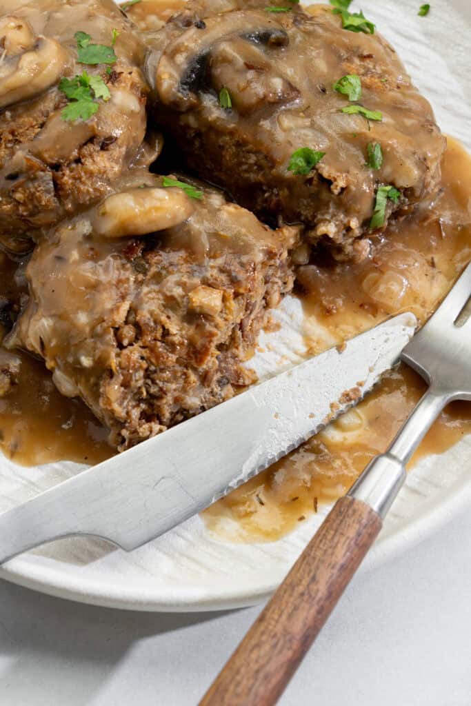 slicing and eating smothered vegan Salisbury steaks revealing its hearty lentil and mushroom filling