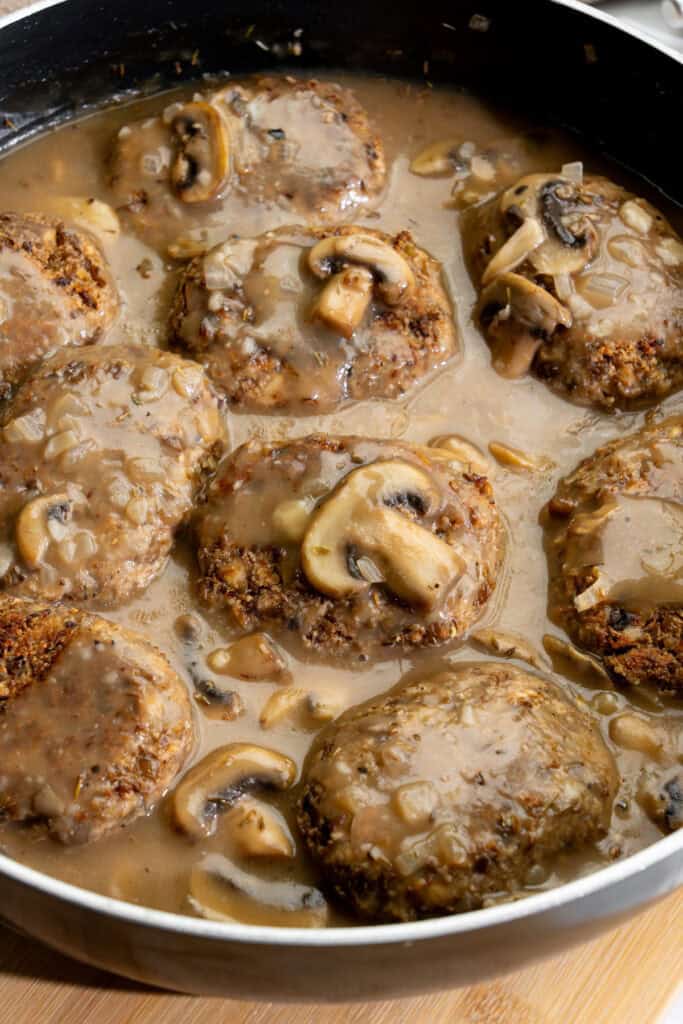 Browned vegan Salisbury steaks in a skillet smothered in mushroom gravy